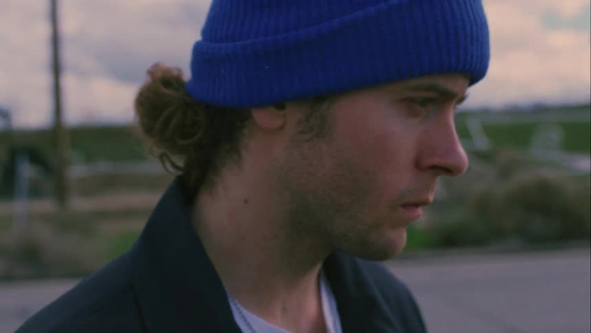A male teenager stands on the side of a road looking mad as cars drive past