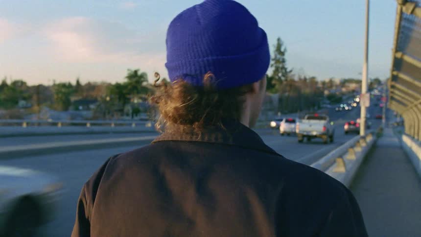 A man walking in a pathway next to a highway with vehicles trees and the sky in the background