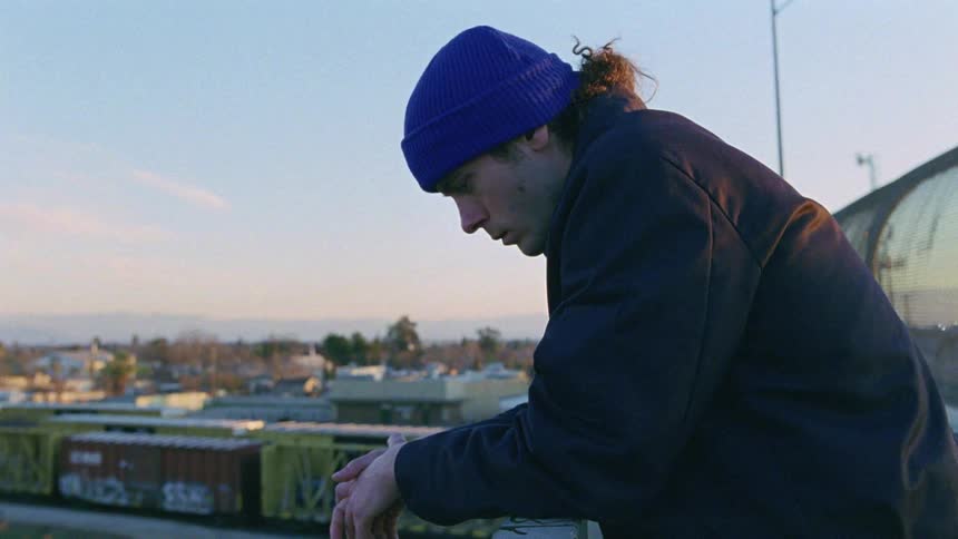Man leans over rail near highway on bridge overlooking stopped train cars