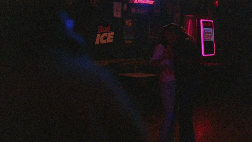A man and a woman slow dancing in a bar with tables and chairs in the background