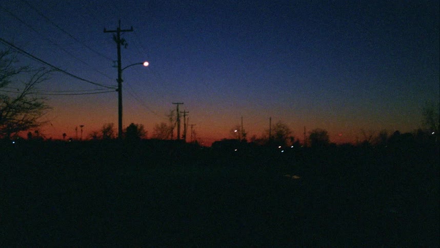 A street with vehicles next to utility poles with the sky and trees in the background