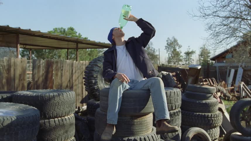 A man climbs some tires and throws a bottle after drinking it