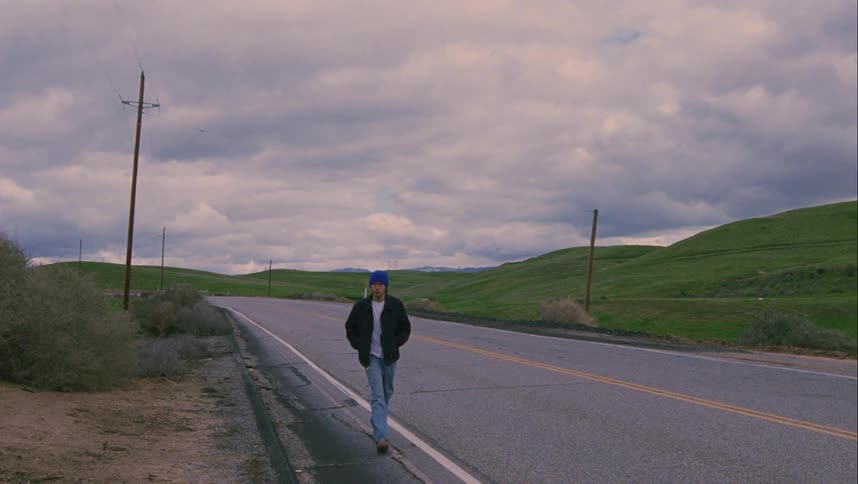 A male teenager walks quickly down the side of a road