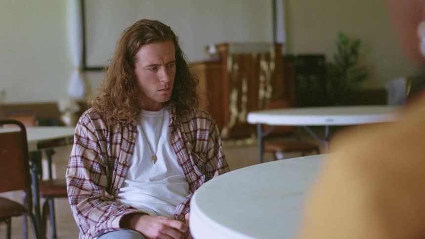 An agitated man fidgets as sits at table across from another person