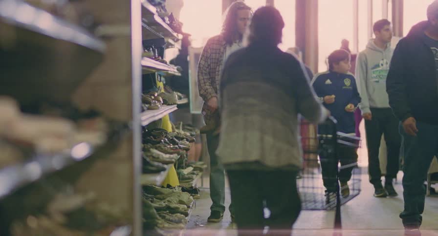 A man tries on shoes in a clothing store while other shoppers walk by