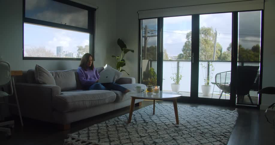 Woman sitting on couch in living room working on her laptop