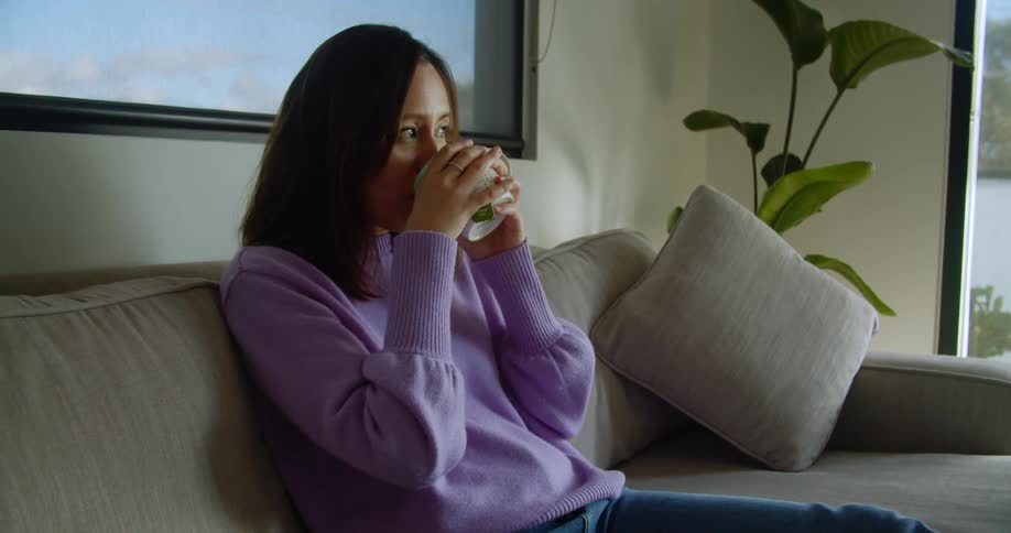 A woman takes a drink from her mug on the couch