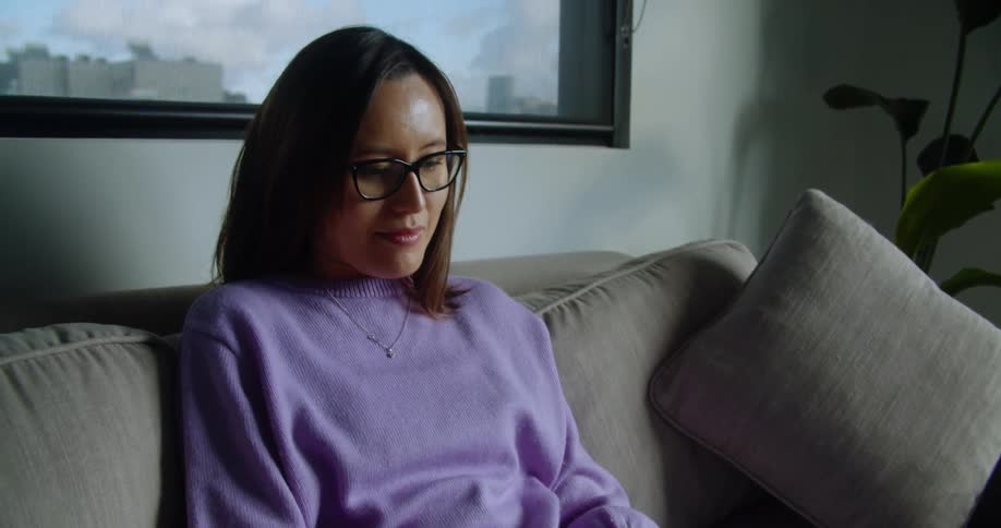 A woman sitting on her couch at home types on her laptop