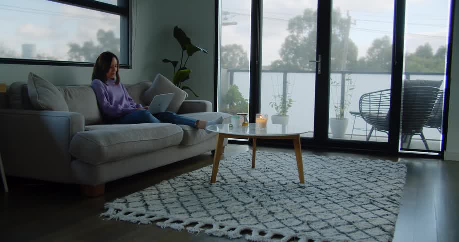 Woman sitting in the couch on the living room types on a laptop