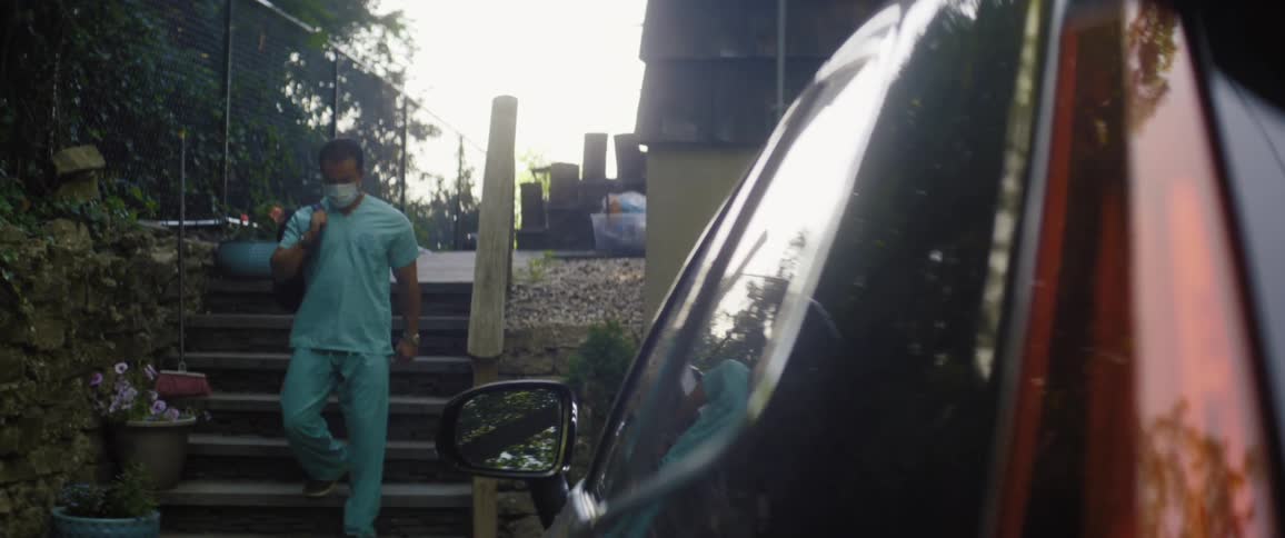 A man with a mask backpack and scrubs walking downstairs with a vehicle in the foreground