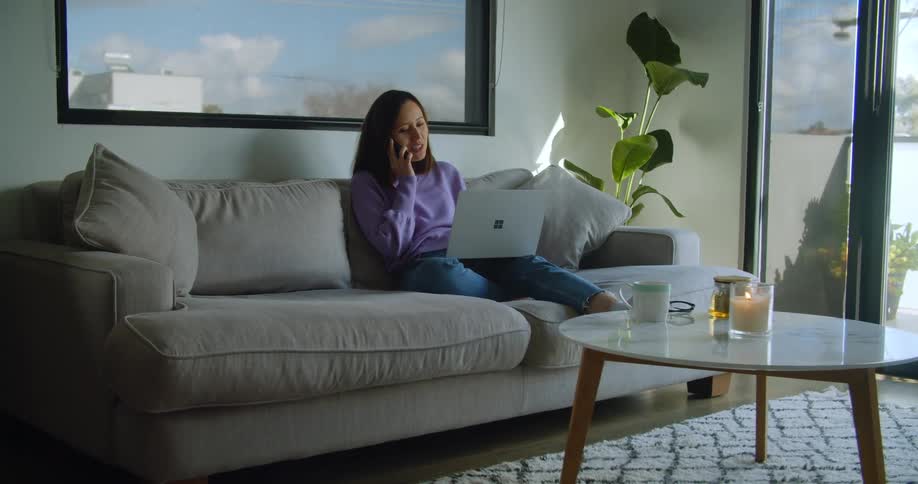 Woman sitting on couch with laptop talking on cell phone