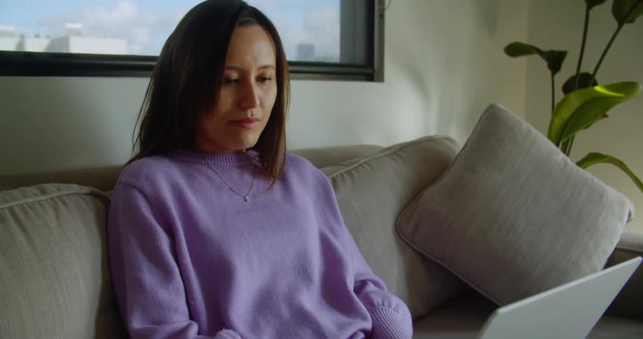 A woman is sitting on her couch typing on a laptop