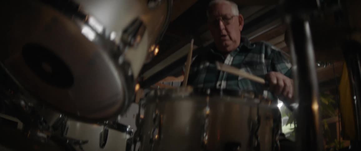 An elderly man plays drums