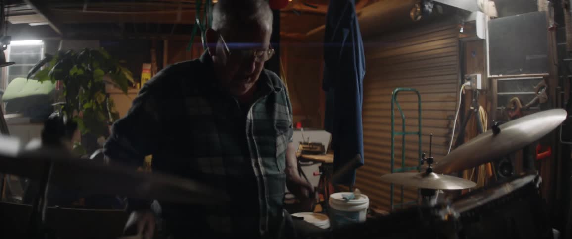An older man is playing drums in his garage
