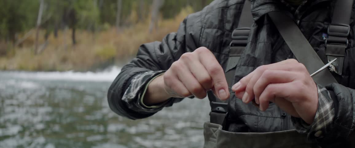 A man is wrapping a lure as he fishes in a river during the day
