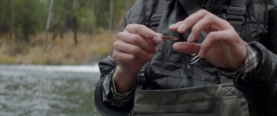 A man is tying a fly to a fishing road in the middle of a lake