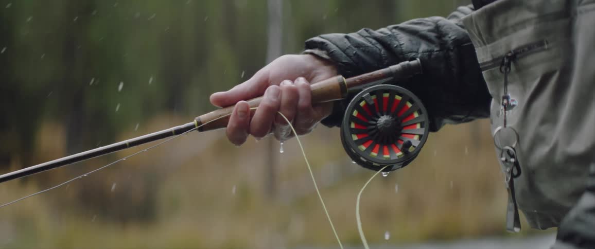 A man is playing out fishing line as he fishes in a river during the day