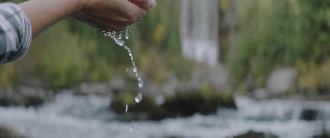 A woman lifts a handful of river water up and lets it flow