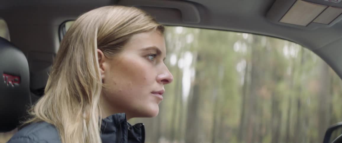 A woman drives down a forest road