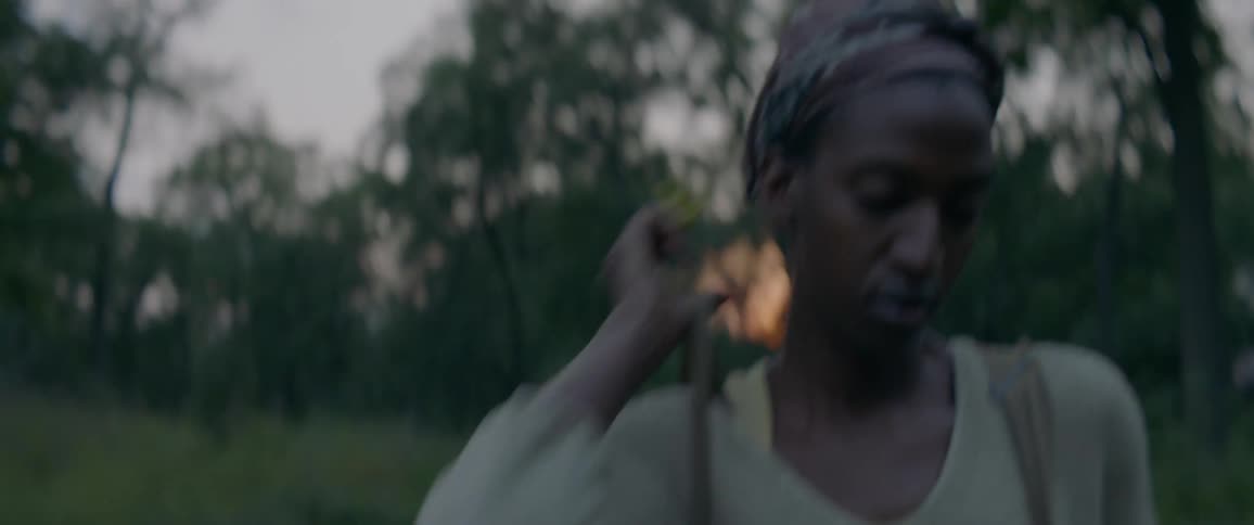 A girl adjusts the straps on her backpack while walking in the woods at sunset