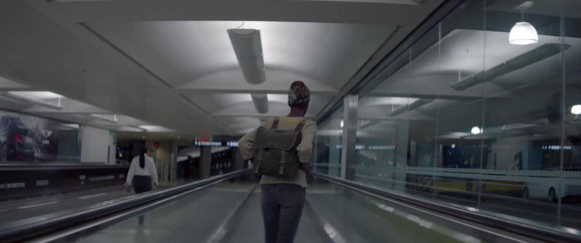 Woman wearing backpack is standing on moving walkway in airport