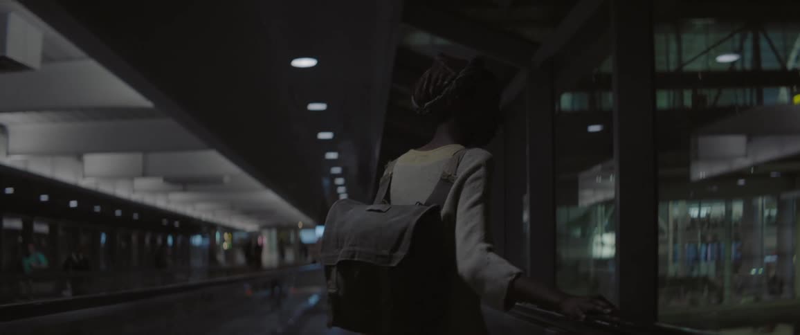 A person wearing a backpack  walks near windows indoors