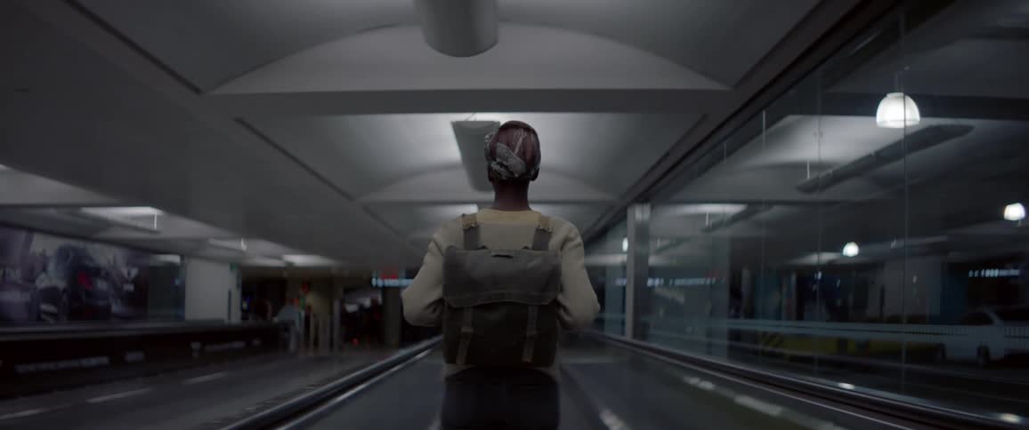 A girl wearing a backpack stands on moving walkway in an airport