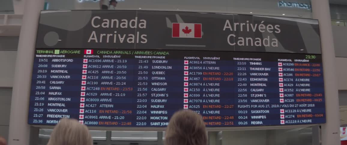 People are looking at an arrivals board in an airport at night