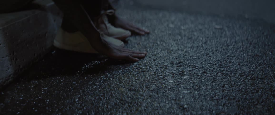 A woman is running her hands over the ground and her sneakers at night