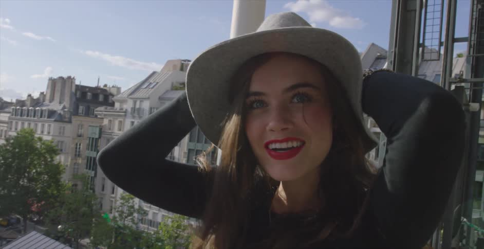 A woman smiles while putting a hat on her head on a sunny day in the city
