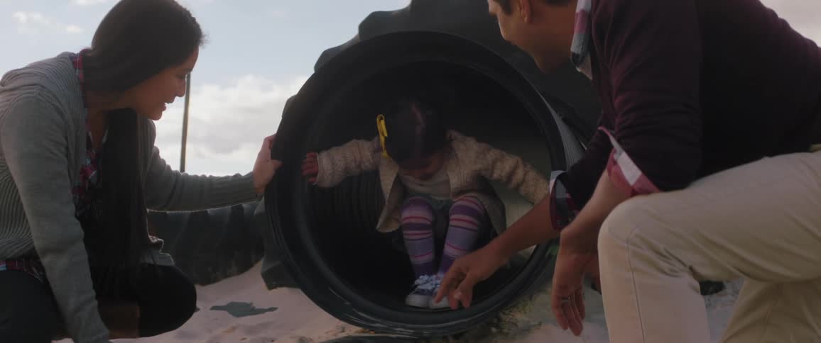 A mother and father watches are their kids are crawling through a tunnel on a playground