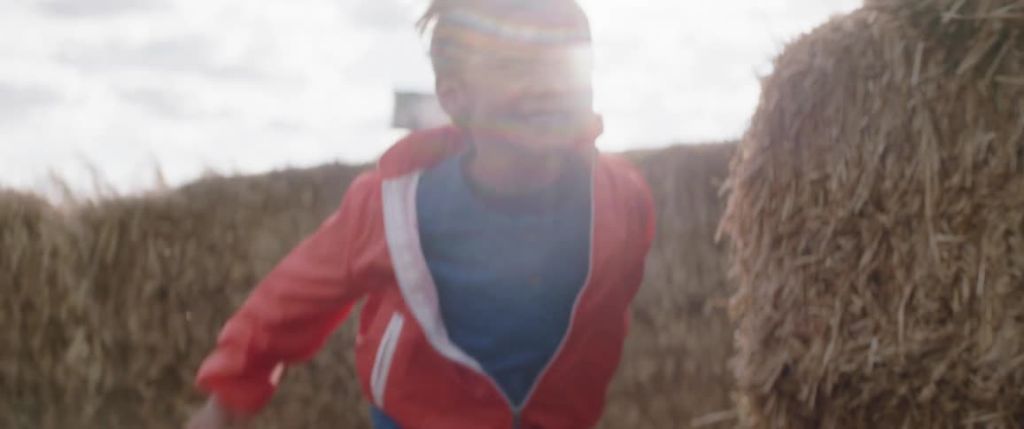 A child in a red jacket is running through a hay maze
