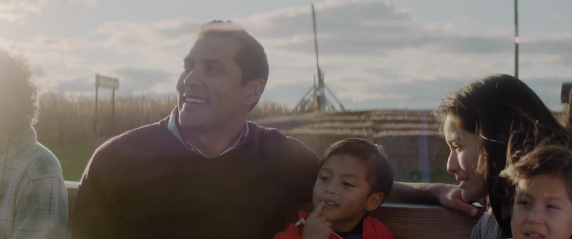 A family rides in the bed of a truck through a corn field