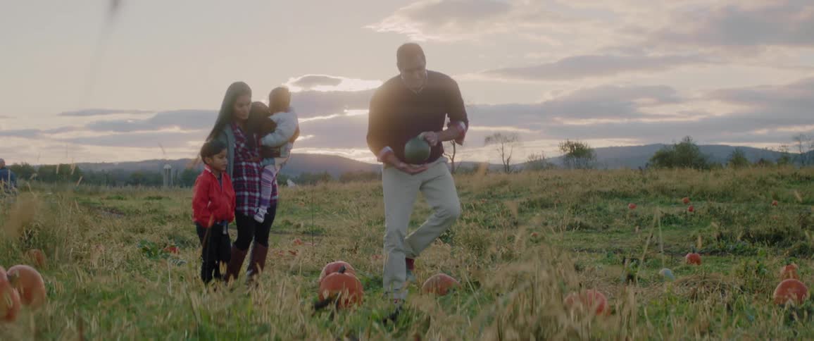 A family is walking in a pumpkin field choosing a pumpkin at dusk