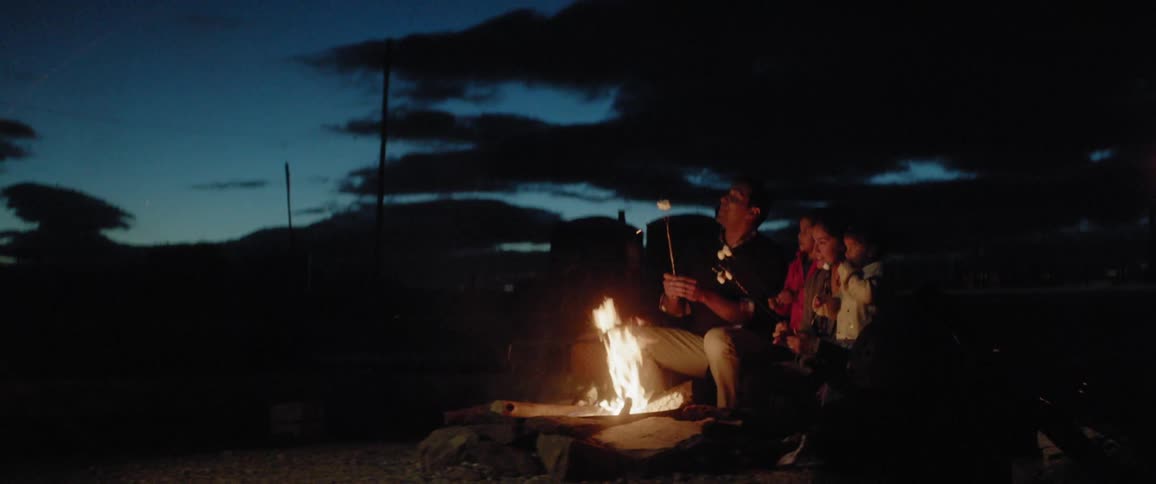 A family are sitting in front of a fire roasting marshmallows