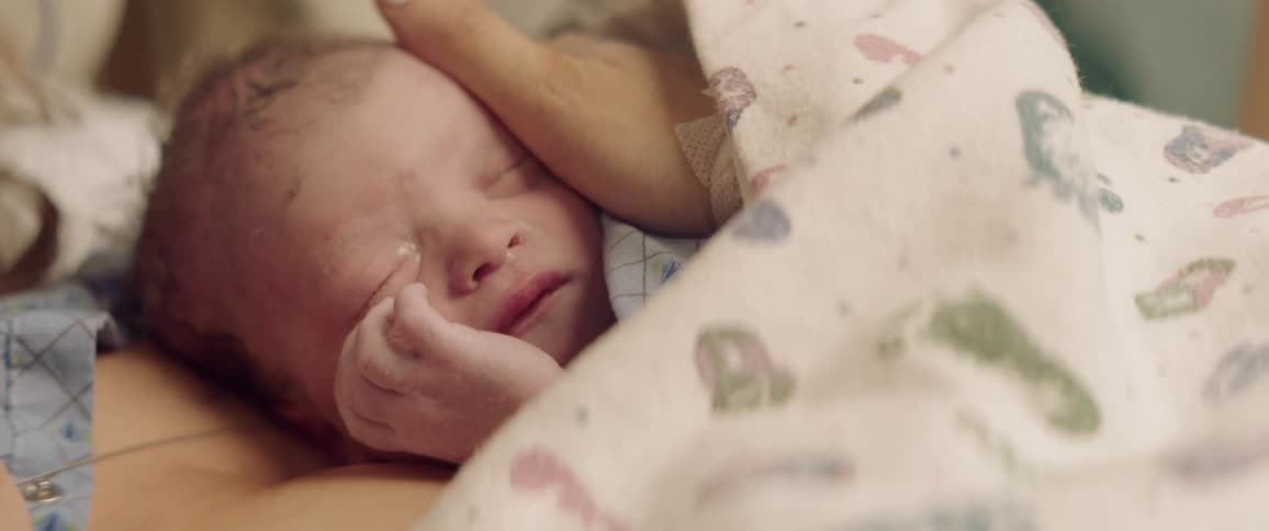 A woman's hand is stroking a newborn's head inside in daylight