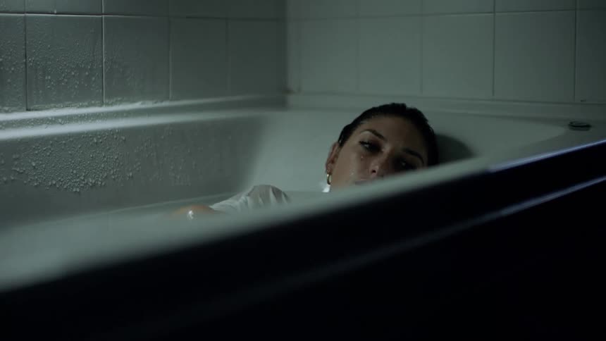 A woman lays in the bathtub fully clothed