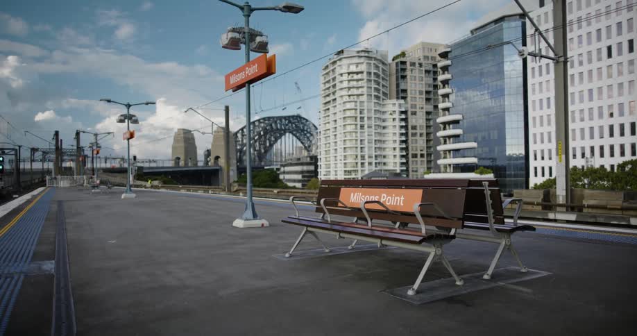 A pair of benches are situated on an open air train station platform in an urban area