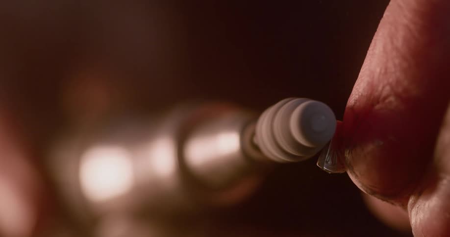 A person carefully uses a rotary tool to smooth the surface of a small jagged object they are holding