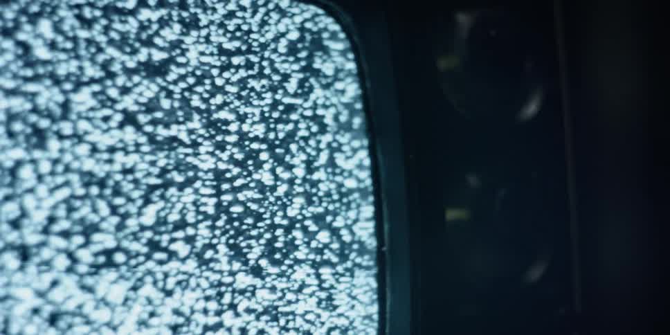 An old fashioned cathode ray television is displaying only static on the screen in a darkened room