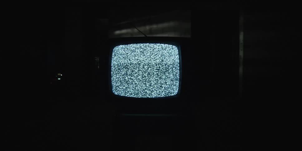 In a dark room an older television set placed on a chair is displaying only static on its screen