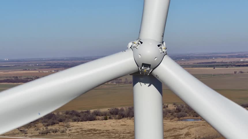 A wind turbine rotating on a wind turbine farm on a grassy plain with the sky and clouds in the background