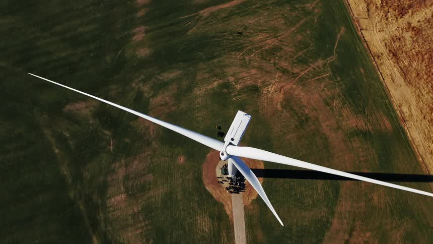 White wind turbine casts shadow on surrounding green field and nearby bare earth