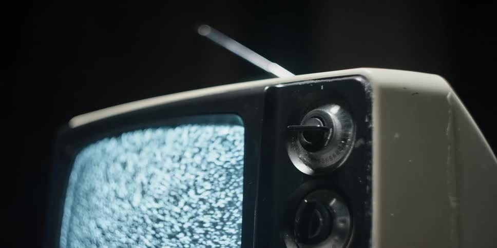In a darkened room an older television set is on and its screen is displaying only static