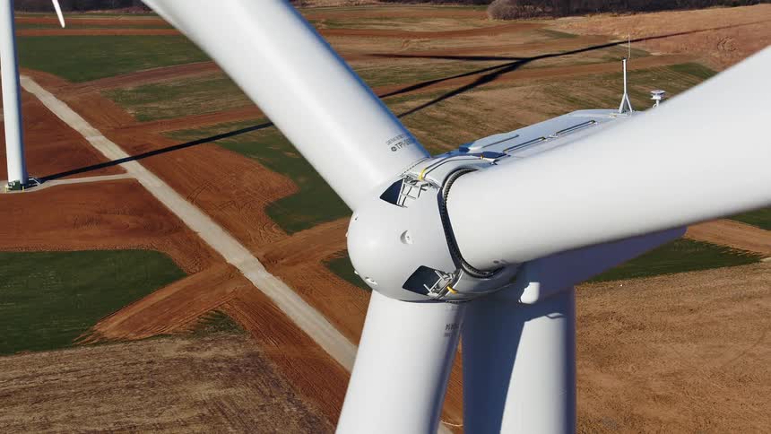 Rotating wind turbines of wind farm cast long shadows onto fields
