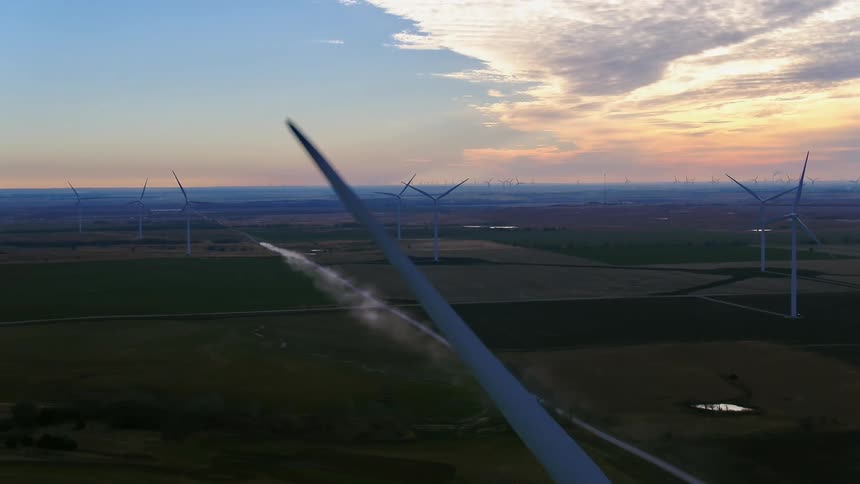 An aerial view of rotating wind turbines on a rural wind farm at sunset