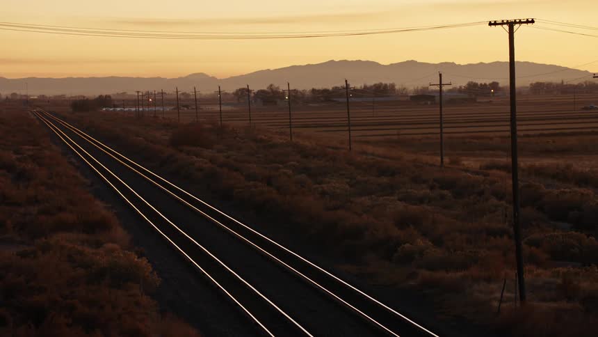 Train tracks next to utility poles with trees mountains and the sky in the background