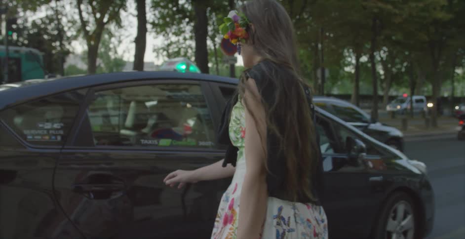 A woman walks over to a car and opens the back door to get in