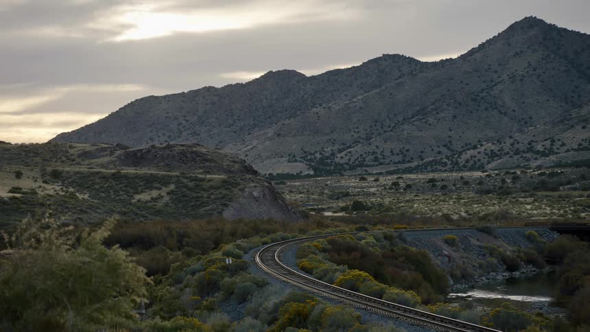A stretch of curved railroad tracks sits before a serene mountain range