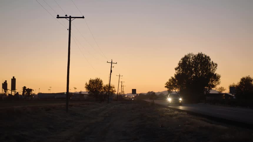 A road with vehicles next to utility poles with trees and the sky in the background
